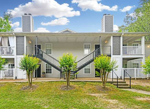 A white two-story house with a grey roof and a balcony on the second floor.