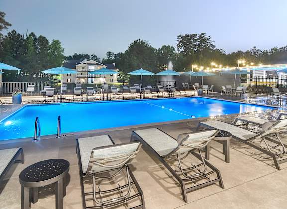 A pool with chairs and umbrellas is lit up at night.