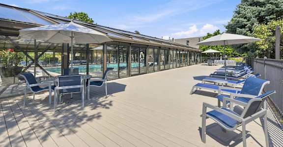 A sunny day at the poolside with blue chairs and umbrellas.