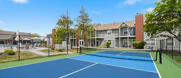 A blue tennis court in front of a residential building.