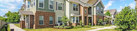 an apartment building with green siding and brick and a sidewalk at Audubon Park Apartment Homes, Zachary, LA