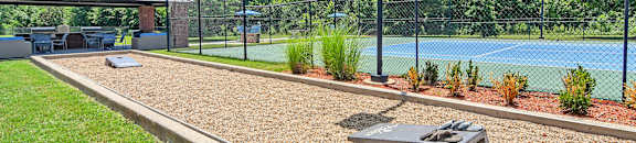 a tennis court with a ping pong table in front of a fence at The Madison Apartment Homes in Tyler, Texas 75703