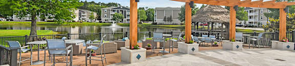 a patio with tables and chairs and a wooden pergola overlooking a lake at Reserve at Gulf Hills Apartment Homes in Ocean Springs, MS 39564
