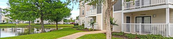 A tree in front of a building with a white fence at Reserve at Gulf Hills Apartment Homes in Ocean Springs, Mississippi 39564