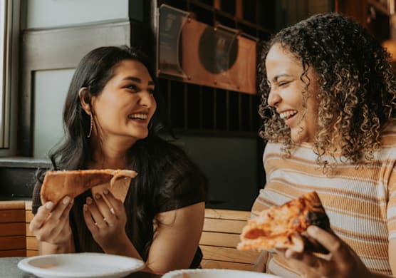 Two people enjoying slices of pizza at a table.