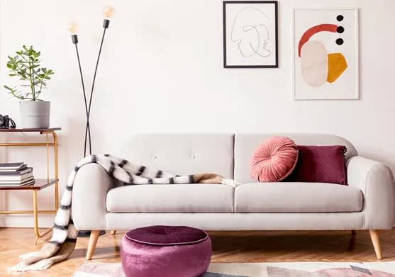 A living room with a grey couch, a purple ottoman, and a small table with a plant on it.