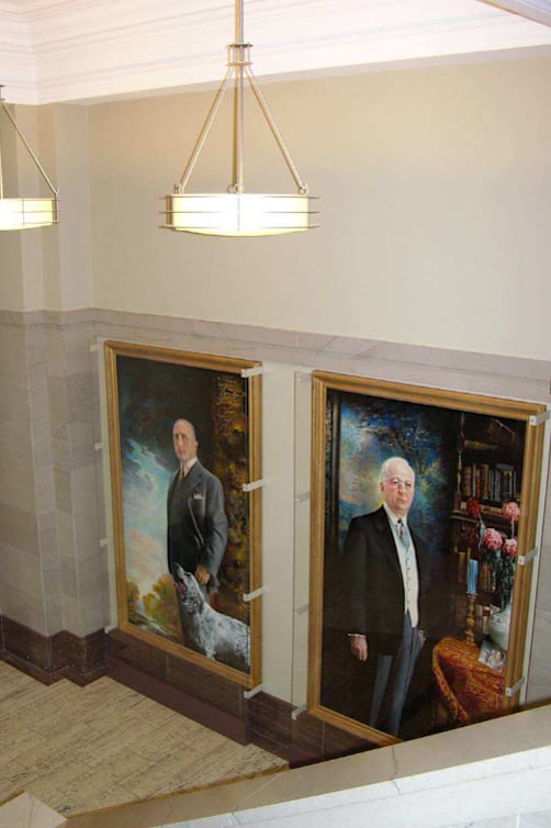 Two portraits of men are hanging in a hallway.