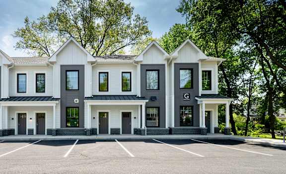 A white building with black trim and windows is surrounded by a parking lot.