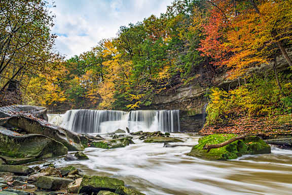 A waterfall surrounded by rocks and trees with autumn leaves.