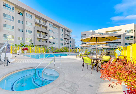 A swimming pool area with a yellow umbrella and chairs.