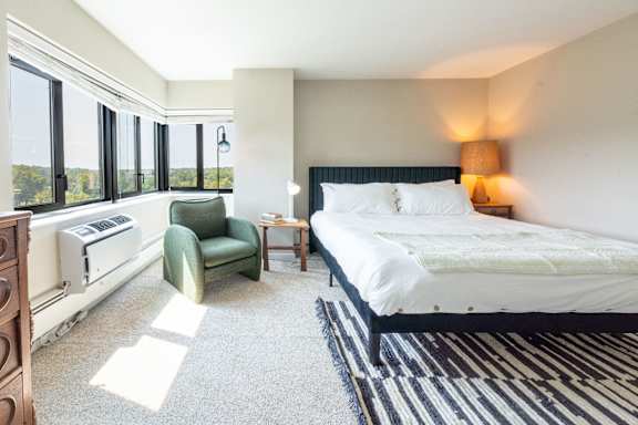 A bedroom with a large bed, a green chair, and a window with a view.