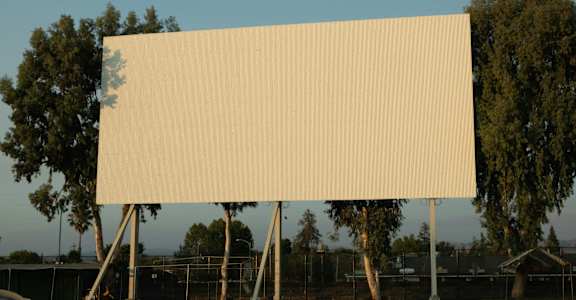 A large blank billboard stands in a parking lot.