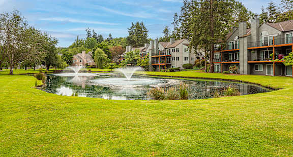 A beautiful residential area with a fountain in the middle of a grassy field.