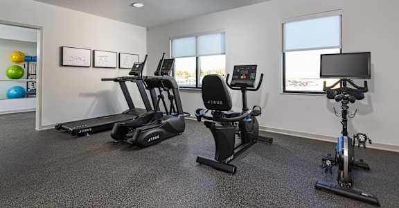 A gym room with a treadmill, exercise bike, and rowing machine.