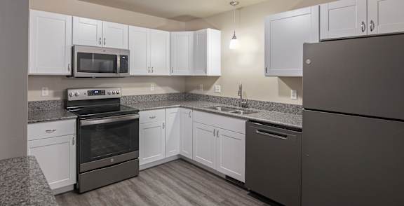 A room with a black fridge and wooden flooring.