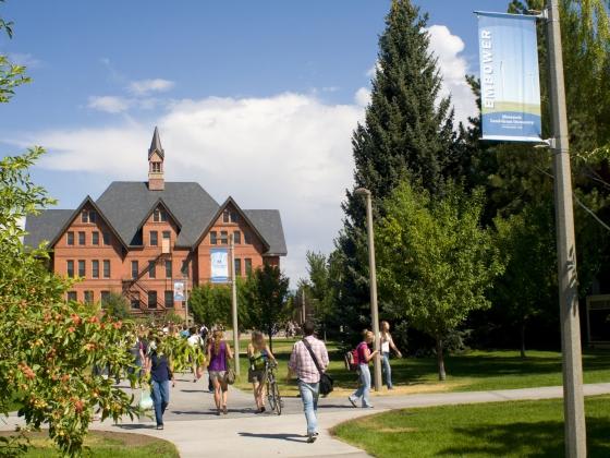 A group of people are walking on a path in front of a large building with a sign that says "ENROLLMENT".