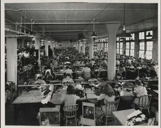 A black and white photo of a factory with workers seated at desks.