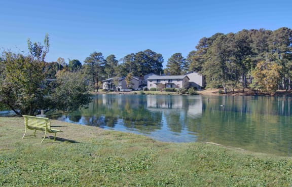 a bench on the grass next to a body of water with a house in the background