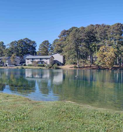 a bench on the grass next to a body of water with a house in the background