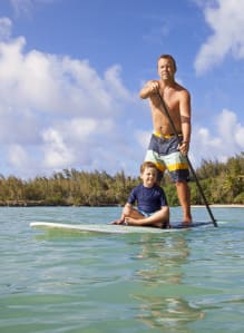 a man and a boy standing on a surfboard in the water