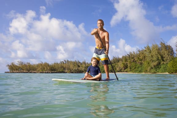 a man and a boy standing on a surfboard in the water