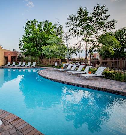 A large outdoor swimming pool surrounded by a brick patio and lounge chairs.