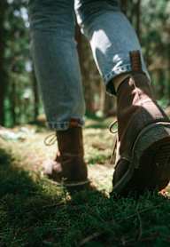 A person is standing in a forest wearing blue jeans and brown boots.