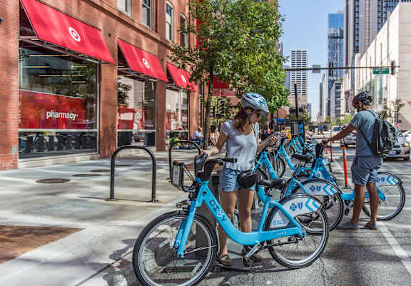 A woman in a white shirt and blue helmet is standing next to a blue bike.