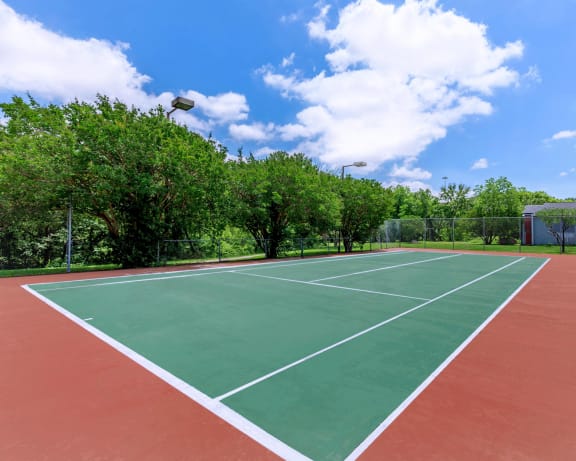 a tennis court with trees and a blue sky with clouds