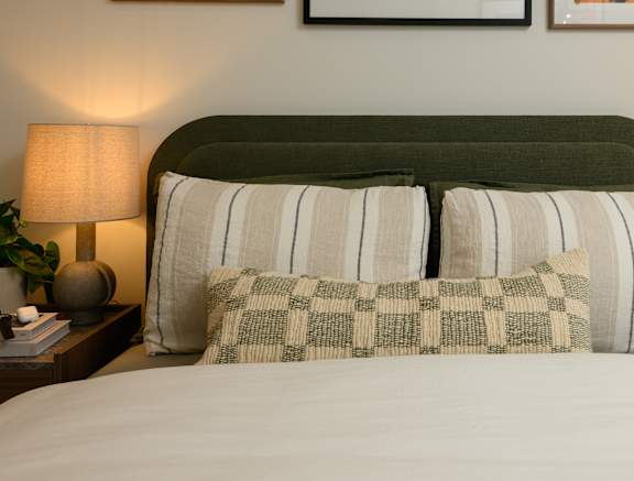 A bed with a green headboard and striped and checkered pillows.