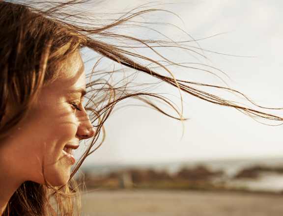 A woman with her hair blowing in the wind on a beach.