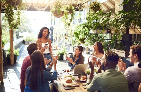 a woman stands in front of a table with a group of people sitting around it