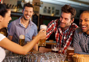 A group of people toasting with beer glasses at a bar.