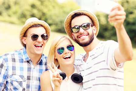 Three friends wearing hats and sunglasses taking a selfie.