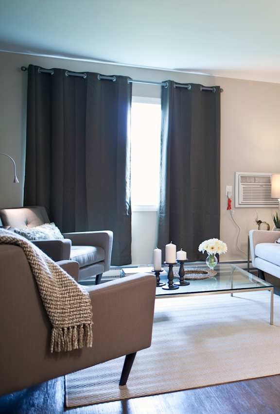 A modern living room with a grey sofa, a glass coffee table, and a large painting on the wall.