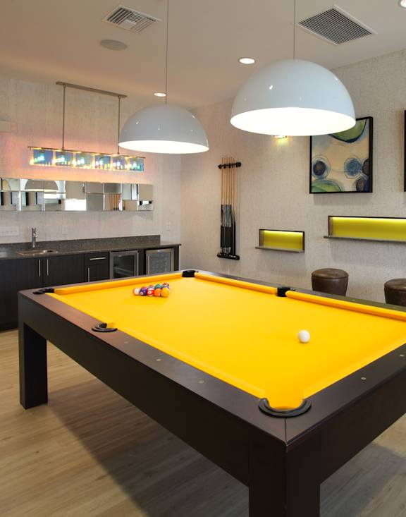 A pool table with a yellow cloth and a white cue ball in the middle.