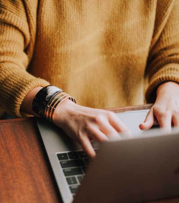 A person in a yellow sweater is typing on a laptop.