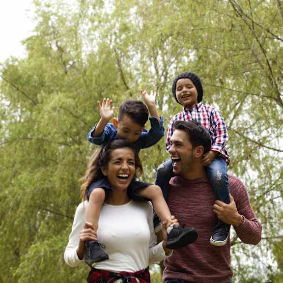 a family walking through a forest with two children on their shoulders at Creekside Canopy, Charlotte, NC
