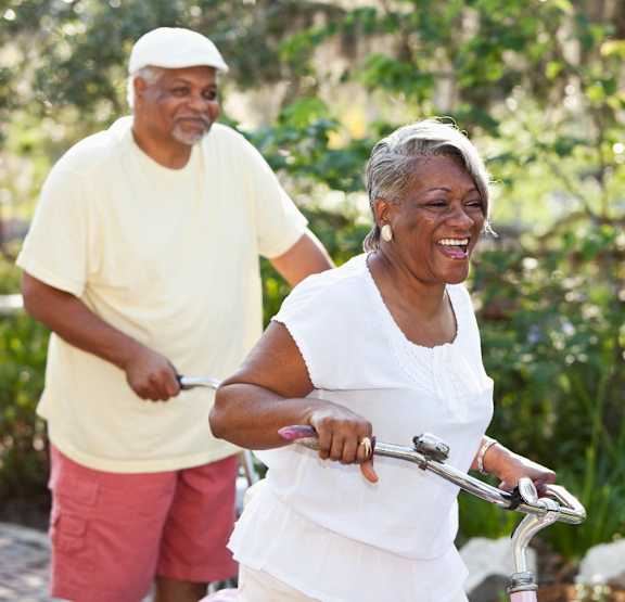 An elderly couple riding a bicycle together in a garden.