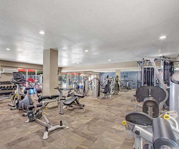 A gym with cardio machines, TVs, and a window view of a pool at Capitol Towers - Towers and Villas. 