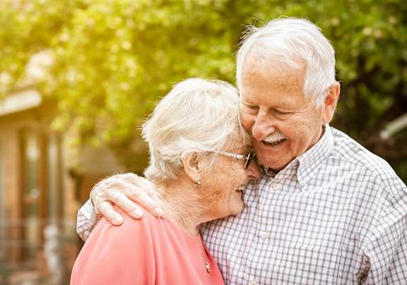 An elderly couple is sitting on a bench in a park.