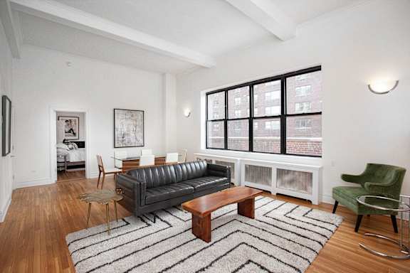 A living room with a black couch, a green chair, and a wooden coffee table.at Sutton Collection, New York New York