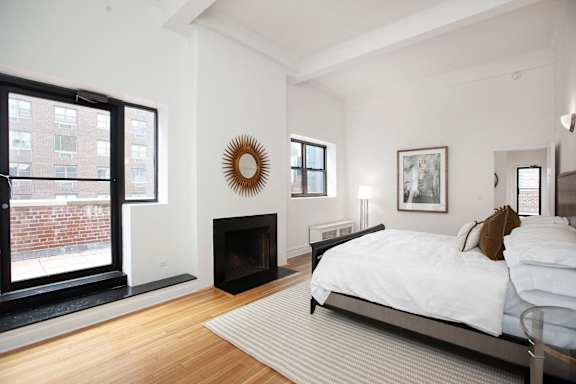 A bedroom with a large bed and a fireplace.at Sutton Collection, New York, 10022