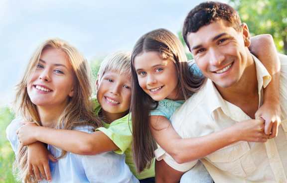A family of four is hugging and smiling together in a park.