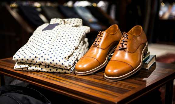 A pair of brown leather shoes and a polka dot shirt on a wooden table.