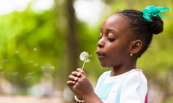 a little girl blowing a dandelion