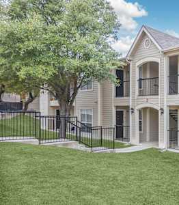 A beige two-story apartment building with a black fence and a green lawn.