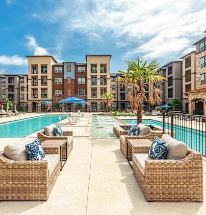 A pool area with wicker chairs and a blue umbrella.