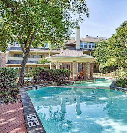 A pool surrounded by trees and bushes with a house in the background.