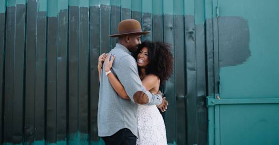 A couple in love hugging against a teal wall.